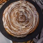 giant cinnamon roll cake frosted and sitting on a black plate