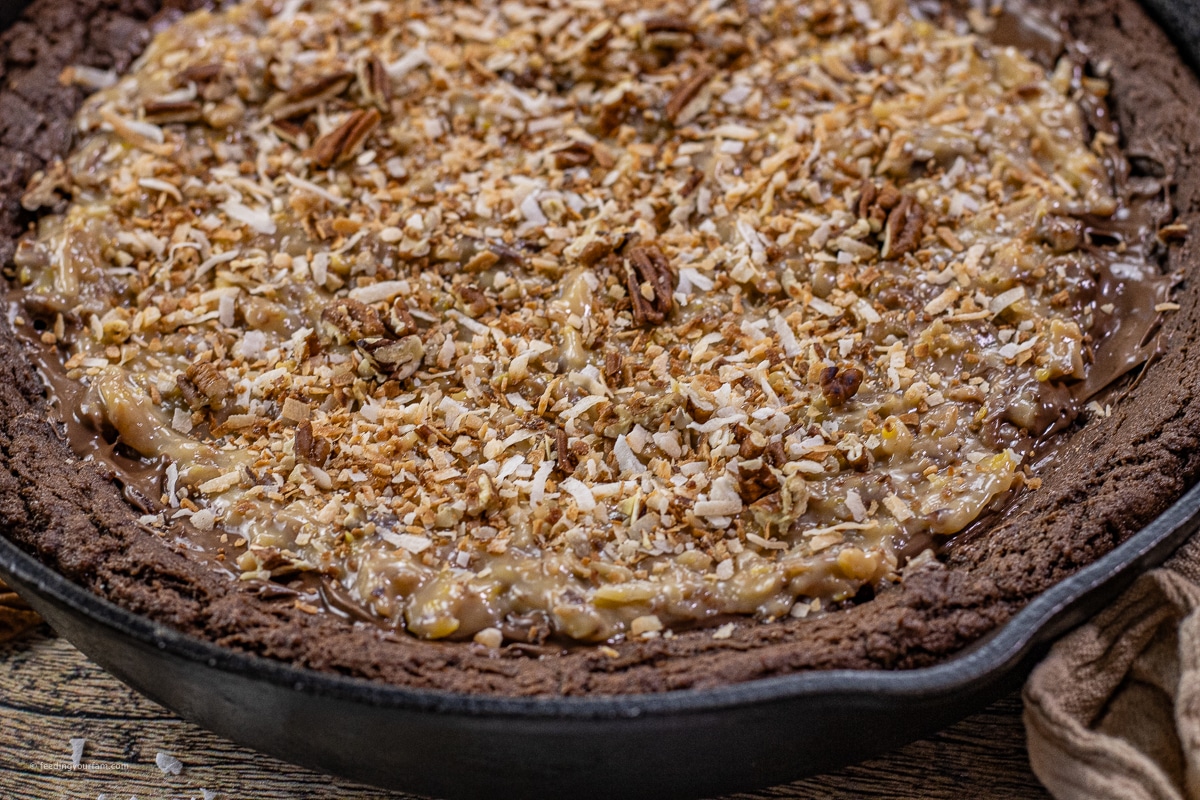 german chocolate cookie baked in a cast iron skillet topped with a coconut pecan frosting