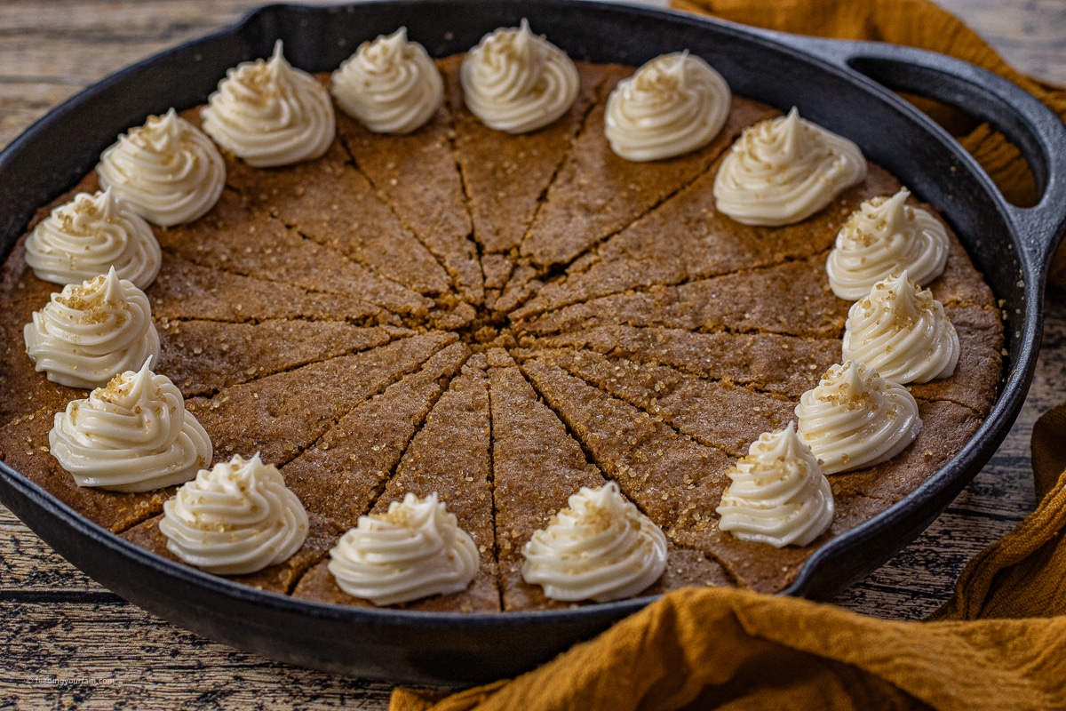 gingerbread cookie baked in a cast iron skillet topped with cream cheese frosting dollops