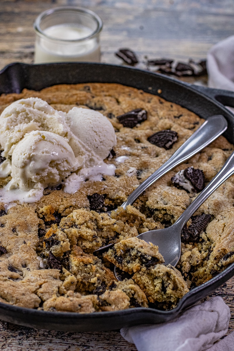 cookies and cream cookie in a cast iron skillet with spoons and vanilla ice cream