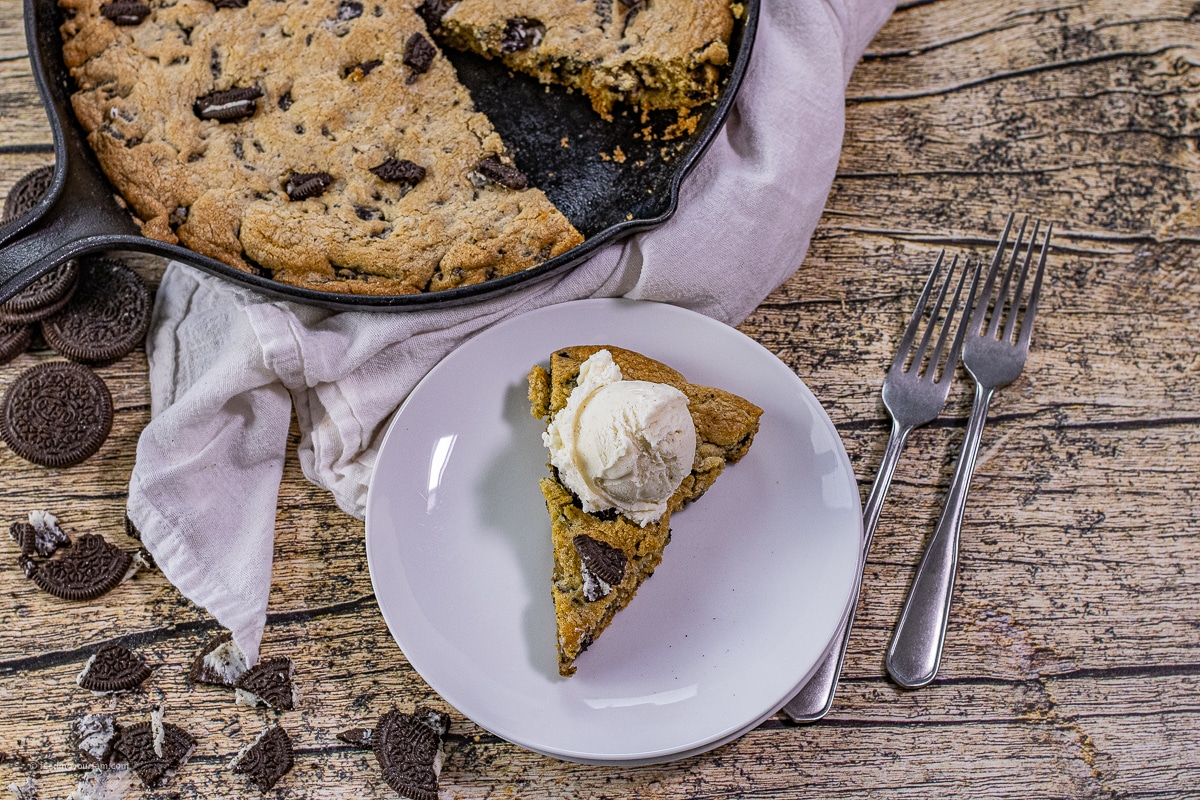 slice of cookies and cream cookie on a white plate topped with a scoop of vanilla ice cream