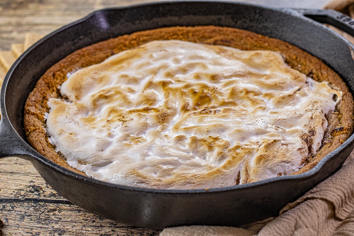 cast iron skillet cookie with a graham cracker crust topped with melted chocolate and a toasted marshmallow