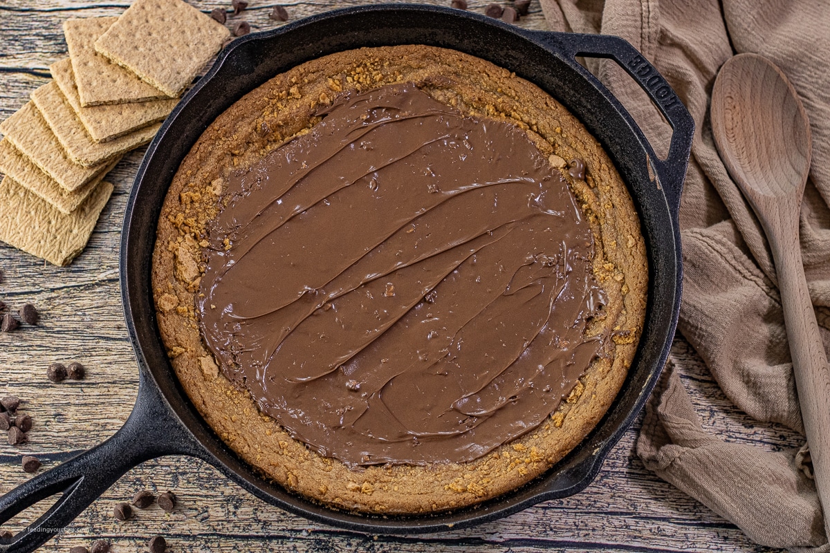 graham cracker cookie in a cast iron skillet topped with melted milk chocolate