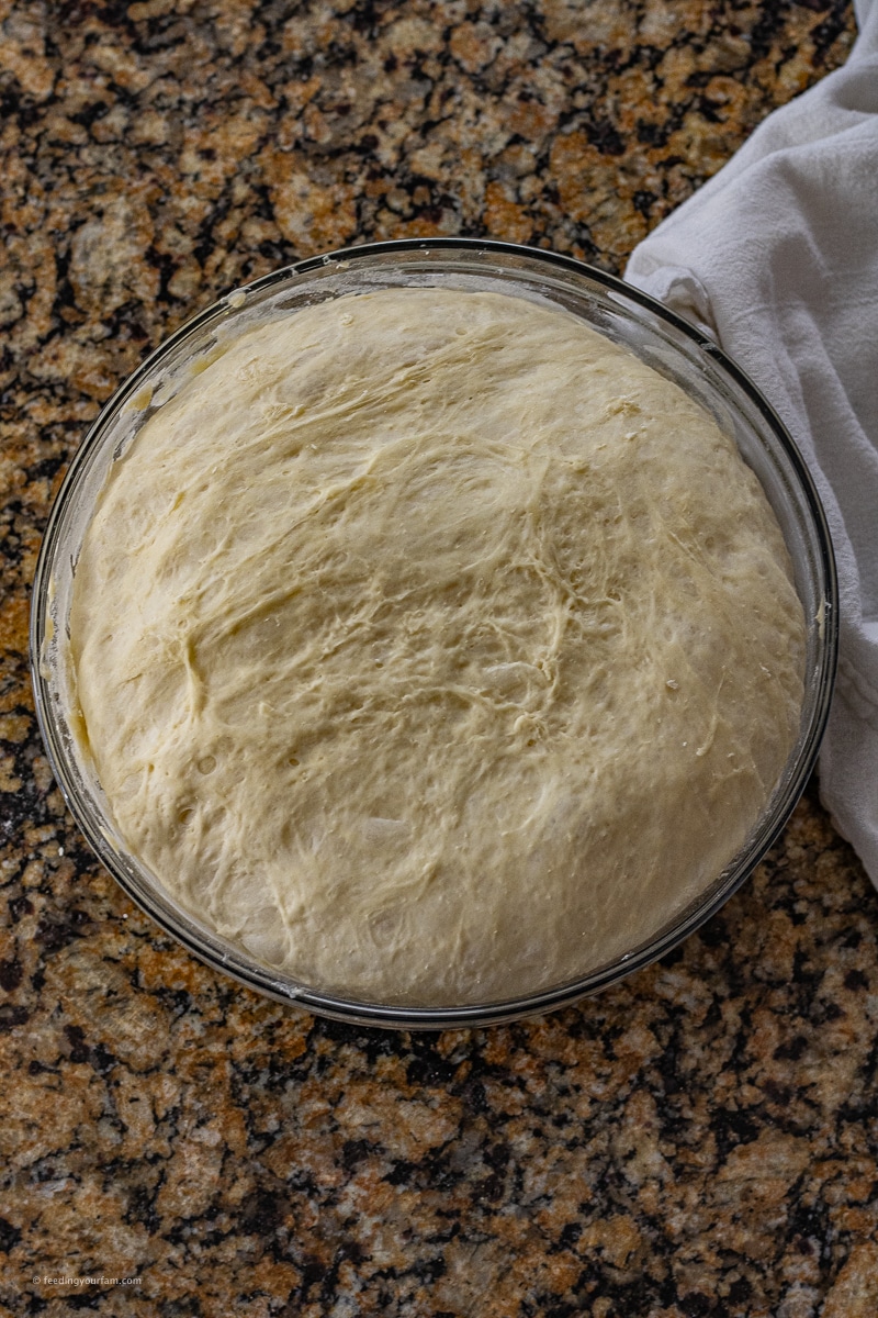 bread dough rising in a glass mixing bowl