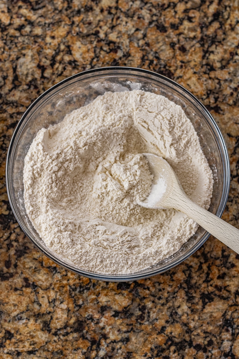 glass mixing bowl with flour and a wooden spoon