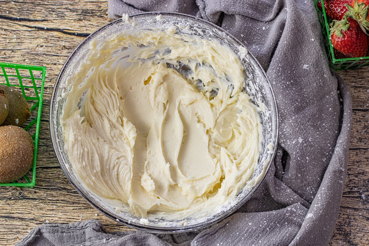 glass mixing bowl filled with freshly made cream cheese frosting for topping fruit pizza