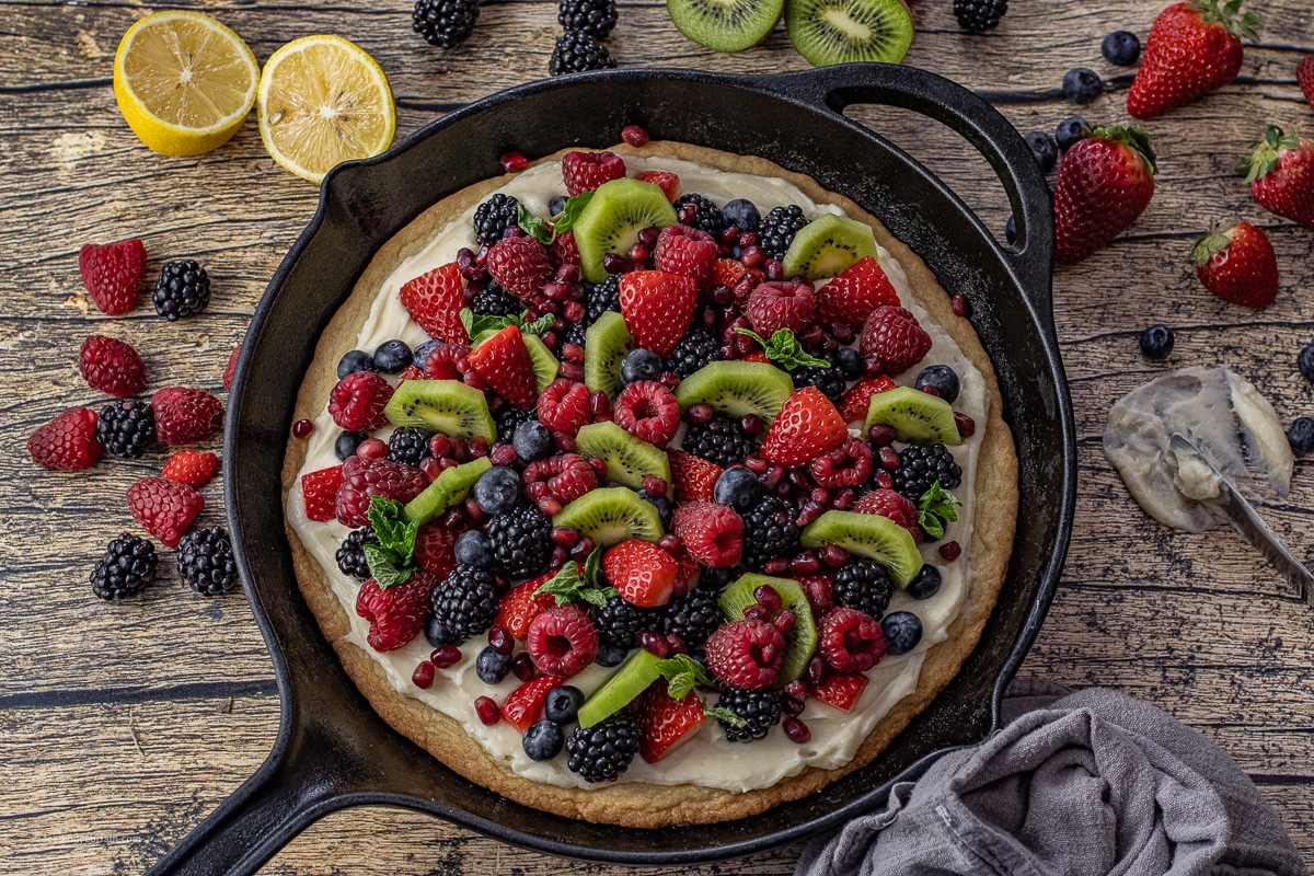 fruit pizza cookie baked in a cast iron skillet topped with fresh berries and sliced kiwi