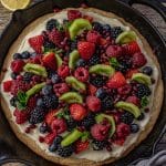 fruit pizza baked in a cast iron skillet topped with fresh berries and kiwi fruit