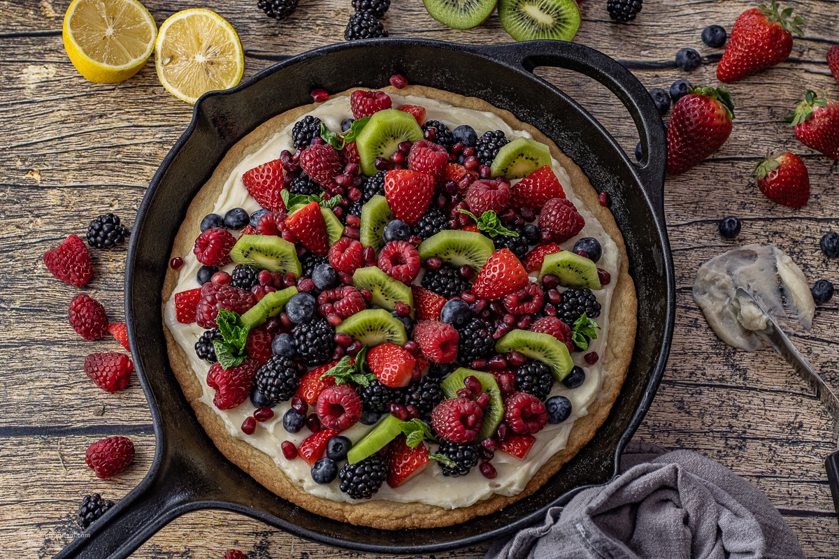 fruit pizza topped with mixed berries and sliced kiwi. The fruit pizza has been cooked in a cast iron skillet