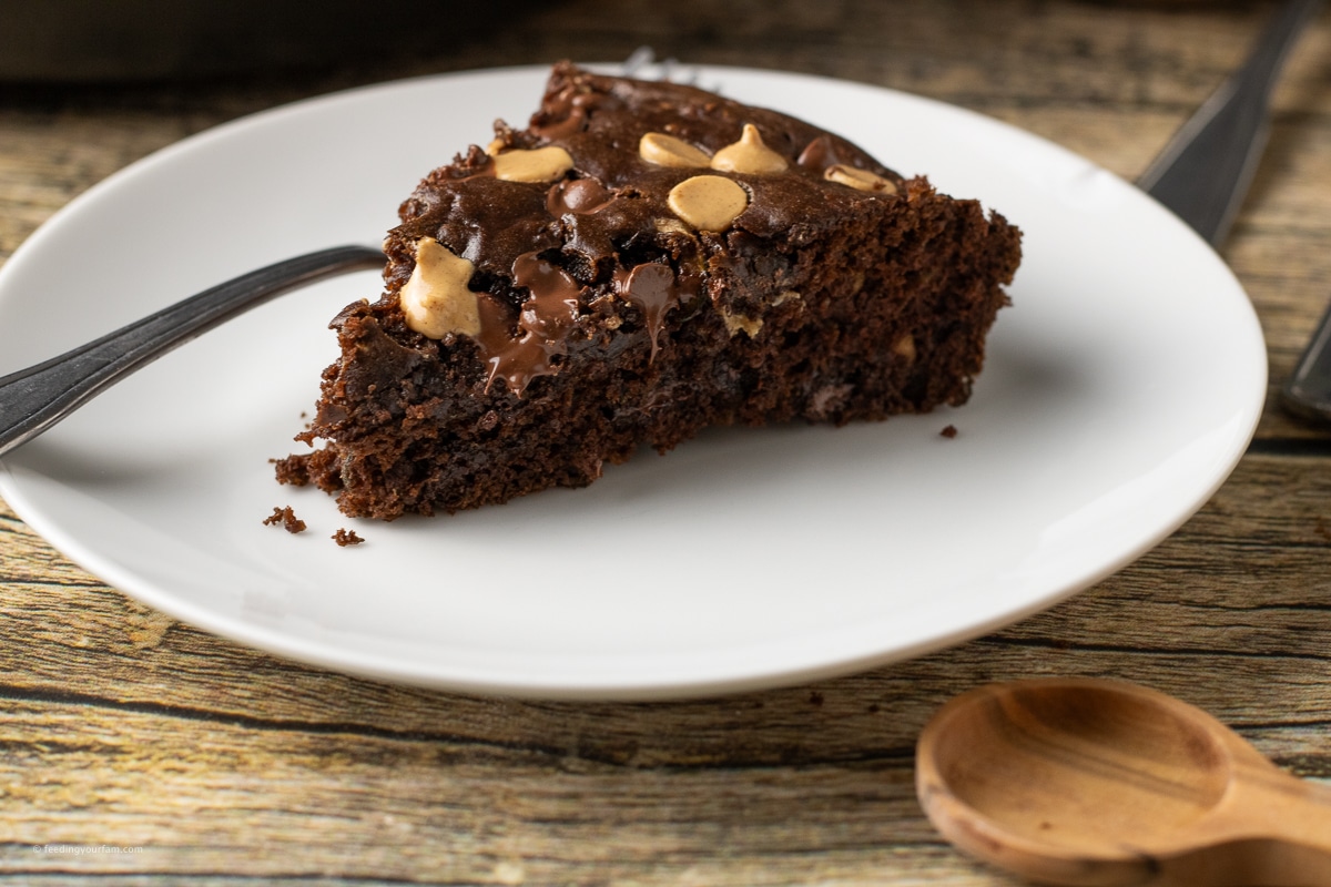 close up shot of a slice of chocolate zucchini bread with chocolate chips and peanut butter chips on a white plate. 