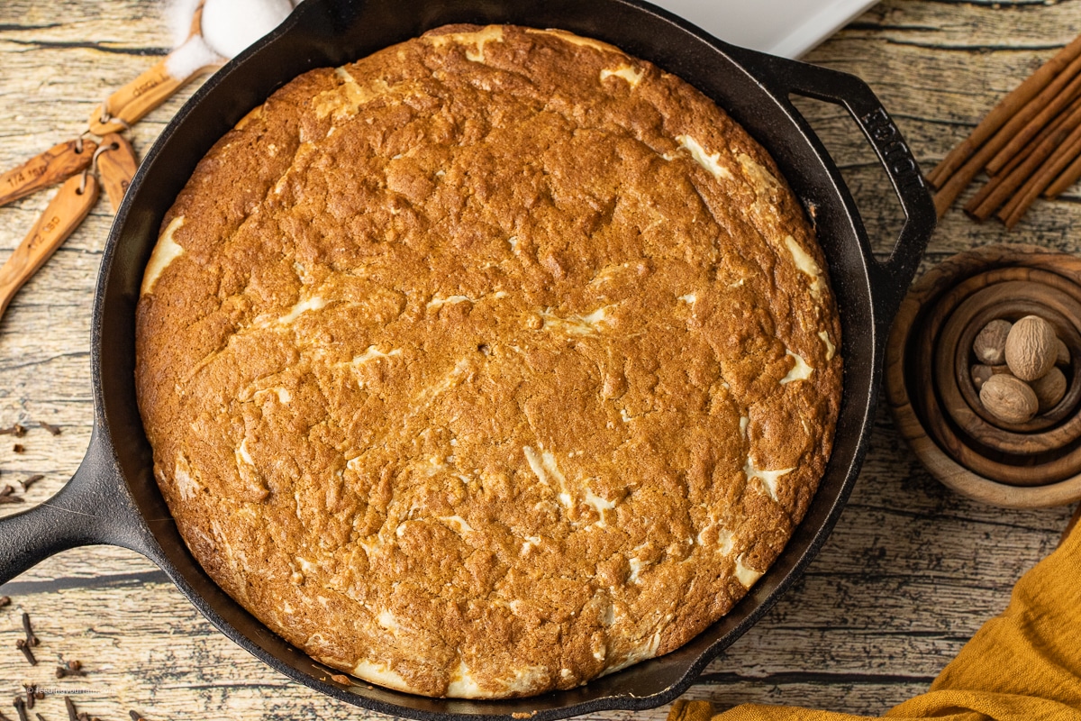 A cast iron skillet filled with a golden pumpkin cookie swirled with creamy cheesecake, baked until soft