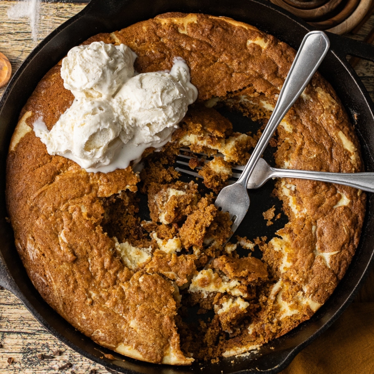 Pumpkin cheesecake skillet cookie topped with cheesecake swirls, baked in a black cast iron pan until gooey in the middle and crisp on the outside.