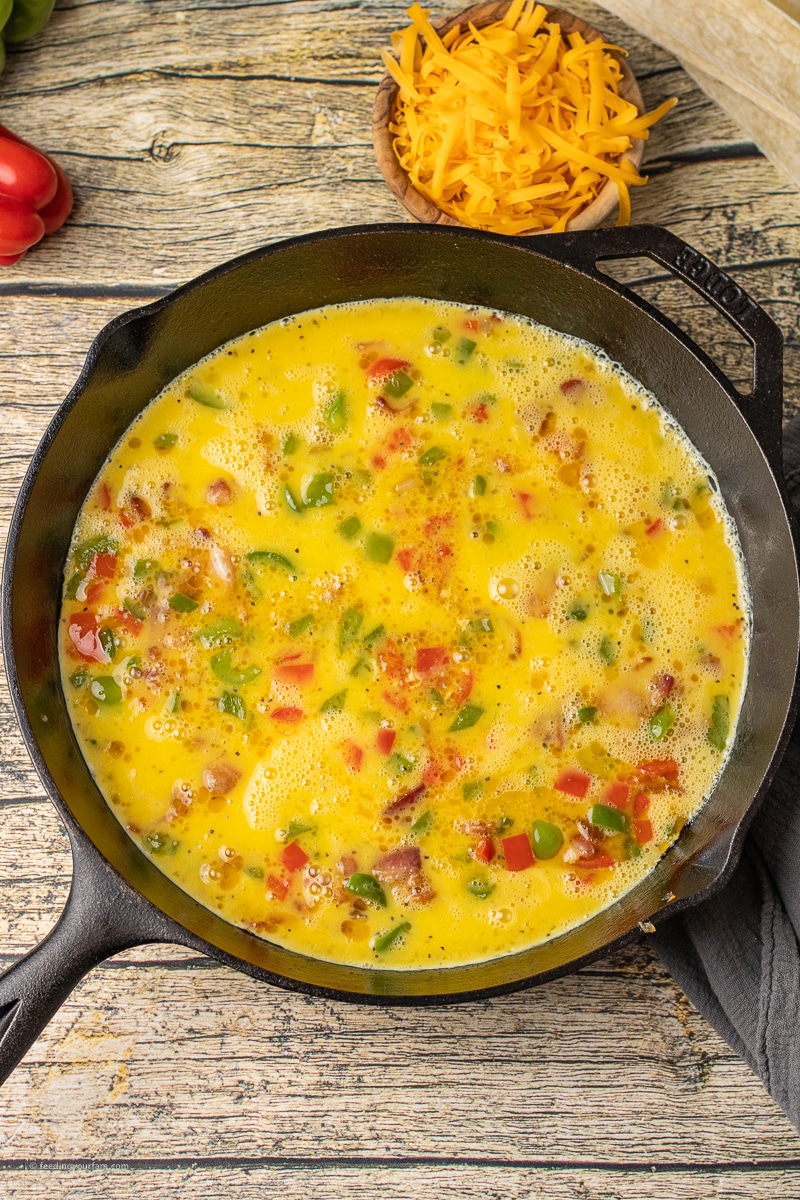 uncooked eggs in a skillet with onions and pepper