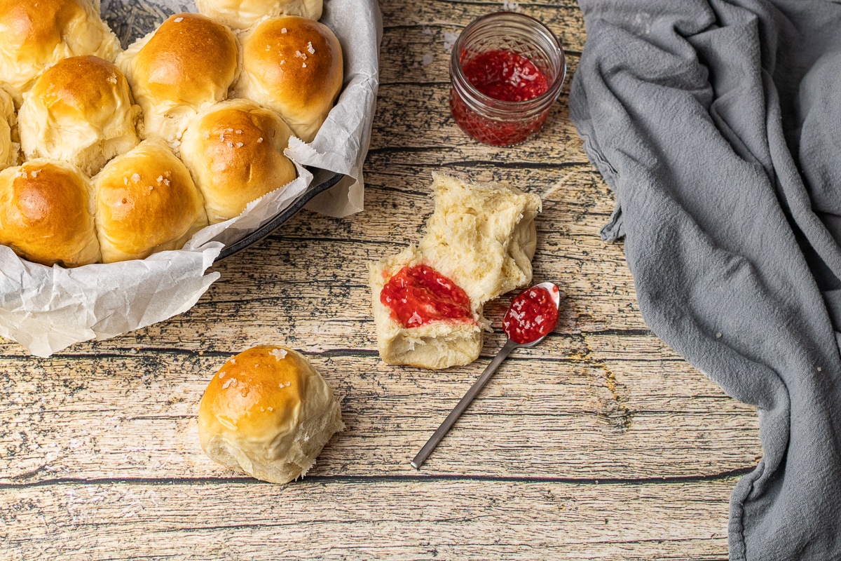 homemade dinner rolls with one split open and topped with jam and butter