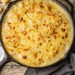 cheesy scalloped potatoes with browned cheese on top baked in a cast iron skillet.