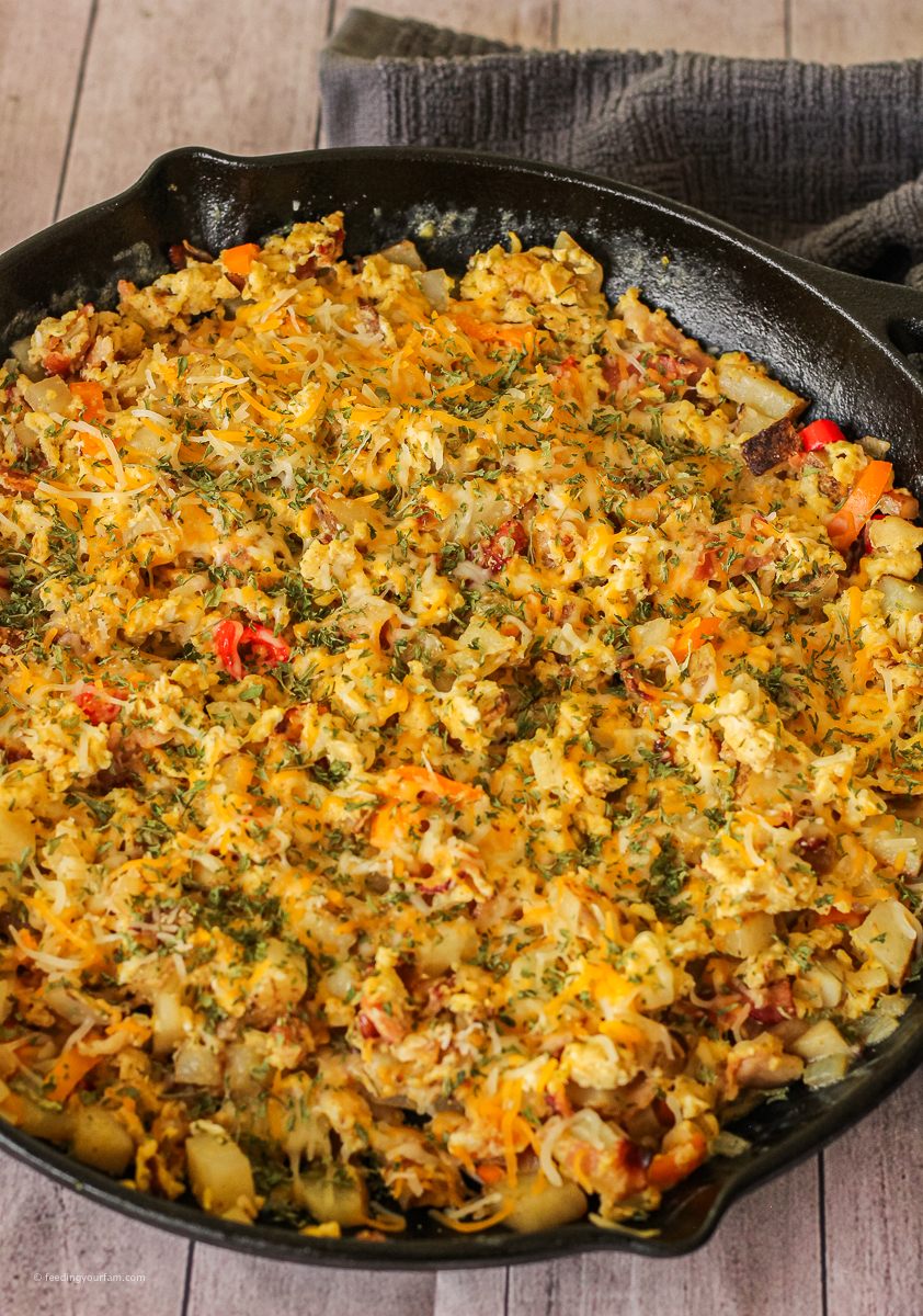breakfast hash with eggs, bacon, potatoes and cheese in a cast iron skillet