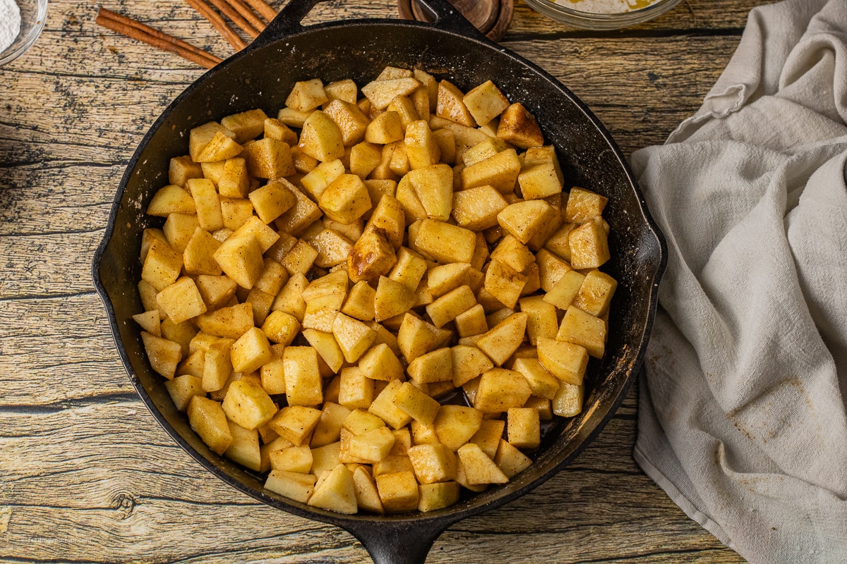 sliced apple coated in a spice mixture placed into a cast iron skillet.