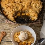 apple cobbler topped with cake like topping with caramel apple filling in a cast iron skillet