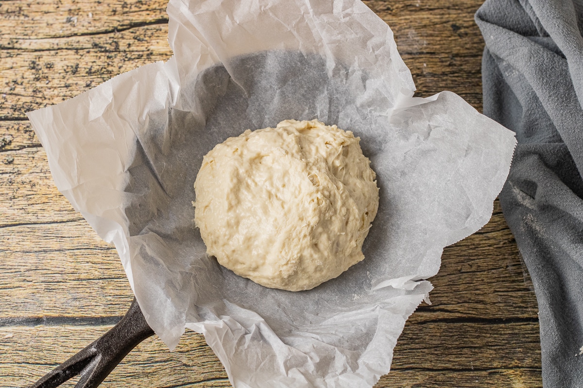 bread dough ball in a small cast iron skillet with parchment paper