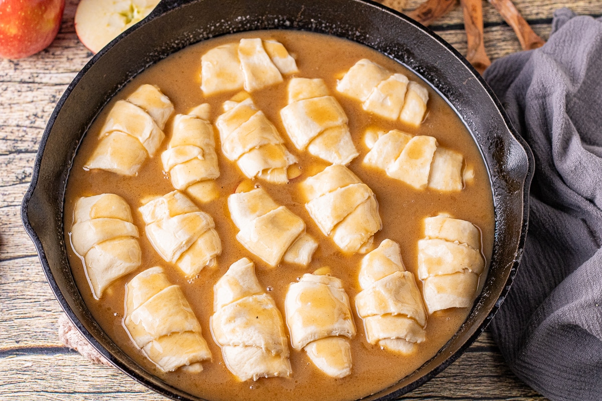 uncooked apple dumplings in a homemade caramel sauce in a cast iron skillet