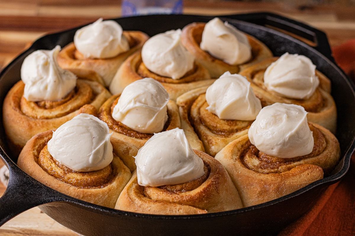 homemade cast iron cinnamon rolls topped with scoops of cream cheese frosting