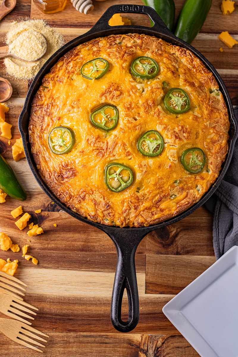 jalapeno cheddar cornbread in a cast iron skillet topped with browned cheese and sliced jalapenos