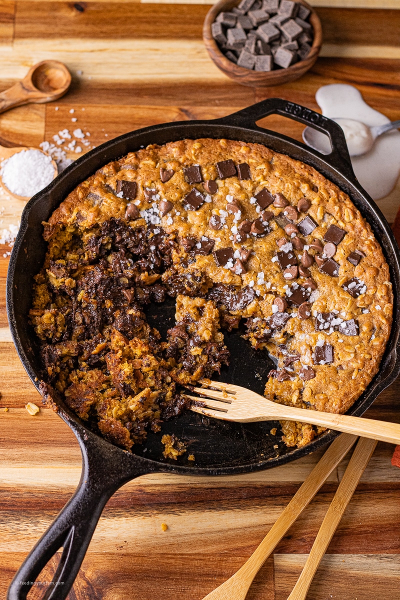 pumpkin chocolate chip oatmeal cookie baked in a cast iron skillet with some of the cookie eaten with a wooden fork in the pan